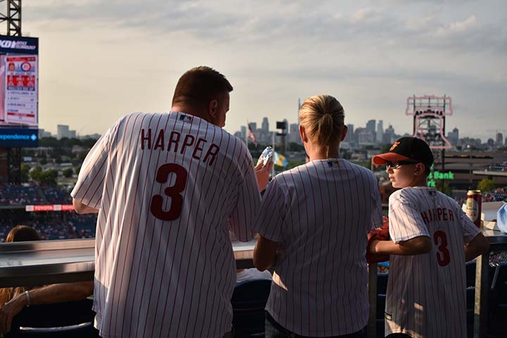 A family watches the game in matching Phillies jerseys while enjoying a hotdog and snacks