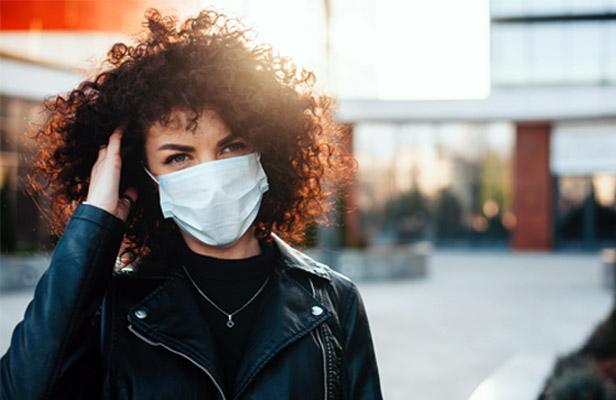 woman with dark curly hair wearing white face mask