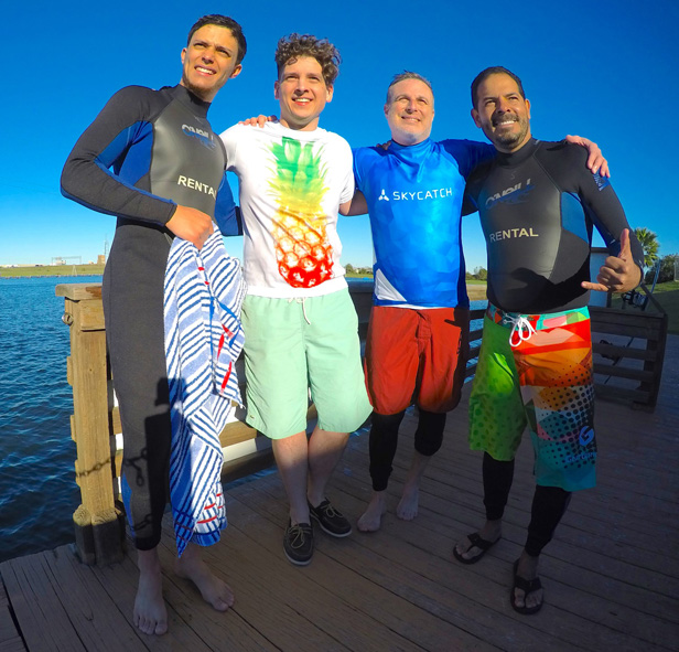 group of men on dock wearing rash guards and wetsuits
