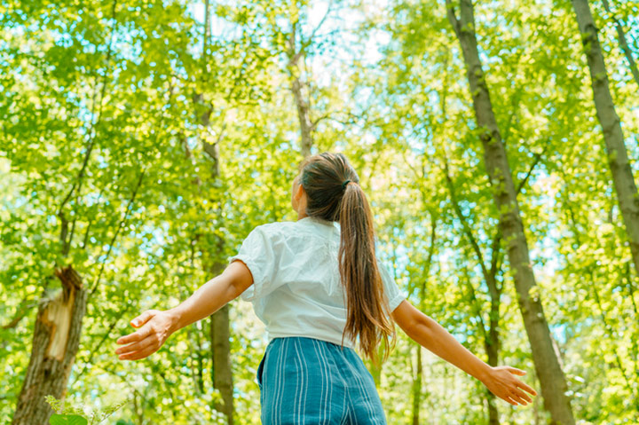 woman with arms outstretched in sunny forest, breathing in the air