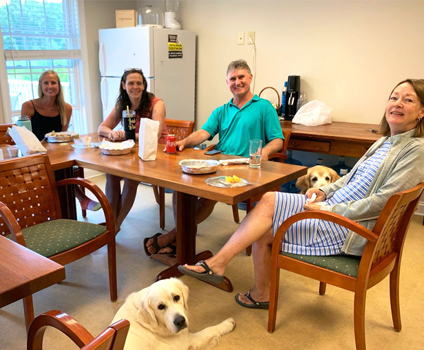 people sitting around table in break room and dog is sitting on floor