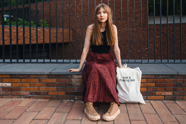 young woman sitting on low ledge next to a reusable tote bag