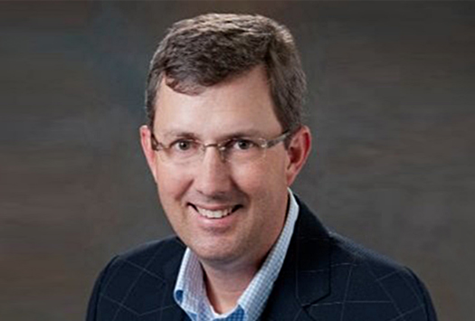 Matt Miller wearing glasses, navy suit and smiling