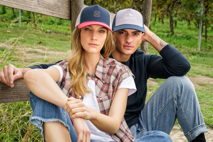 woman and man sitting next to each other against fence, wearing caps