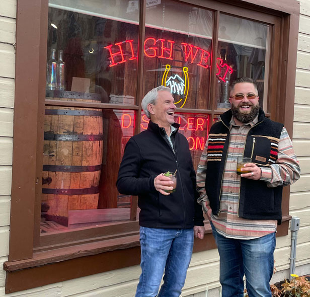 Logomotion owners, two men laughing holding drinks in front of window