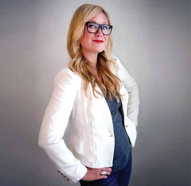 Jill Albers, blond woman standing with hands on hips, wearing white jacket, dark glasses, smiling