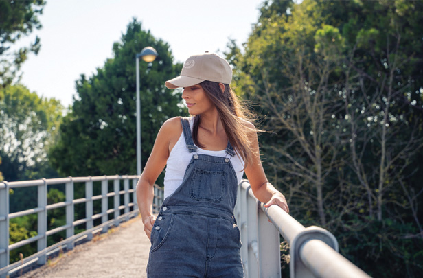 woman in overalls and tan cap, standing on bridge